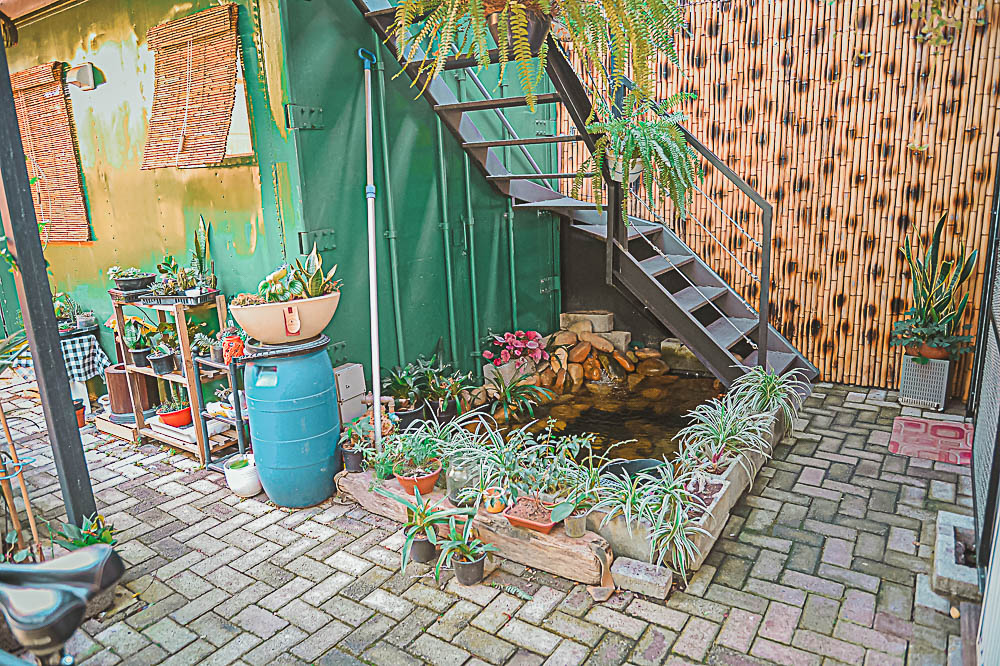 Green steel shipping container reborn as a home, with garden and water feature